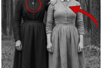 It was just a portrait of a mother and daughter until you noticed the necklace they both wore.  The photograph arrived at Sarah Chen’s office on a Tuesday morning in March 2024, tucked inside a worn cardboard box that smelled of attic dust and old paper.  Sarah, a medical historian at Boston University, had seen thousands of historical images throughout her career.  But something about this one made her pause before she even removed it from its protective sleeve.  The image showed two women standing outside a modest wooden house.  Their expressions serious in the way people posed for cameras in 1887.  The older woman, perhaps in her 40s, wore a simple dark dress with a white apron.  Her hands, rough and capable, rested on the shoulders of a younger woman, barely 20, who stood beside her with the same determined set to her jaw.  Both had dark hair pulled back severely, and both stared directly at the camera with an intensity that seemed to reach across more than a century.  But it was the necklace that caught Sarah’s attention.