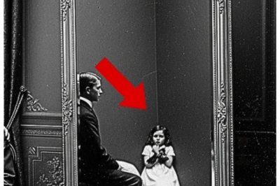 Look Closer: The Mirror in This 1907 Studio Photo Holds a Terrifying Truth  [Music] The Maryland Historical Society’s photography archive smelled of old paper and preservation chemicals.  Thomas Rivera had spent 15 years cataloging Baltimore’s photographic history, handling thousands of glass plates and faded prints that documented the city’s past.  The Thornon Studio collection had arrived.  Three weeks ago, three boxes of immaculately preserved photographs from one of Baltimore’s premier portrait studios, operating from 1895 to 1920.  Thomas has been working through them methodically, recording details about each image, subjects, dates, locations, technical notes.  He removed another large format photograph from its protective sleeve, a formal family portrait, typical of the era.  The lighting was professional, the composition carefully arranged.  The photograph showed four people posed in an elegant studio setting.  Heavy velvet drapes framed the scene.  An ornate Barack mirror with an elaborate gilded frame hung prominently on the back wall, positioned slightly to the left at an unusual angle.  At the center stood a tall, distinguished man in his 40s, wearing a dark suit, his expression stern and authoritative.